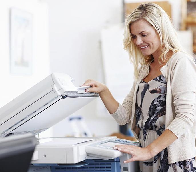 Image features a woman smiling while using a fax machine